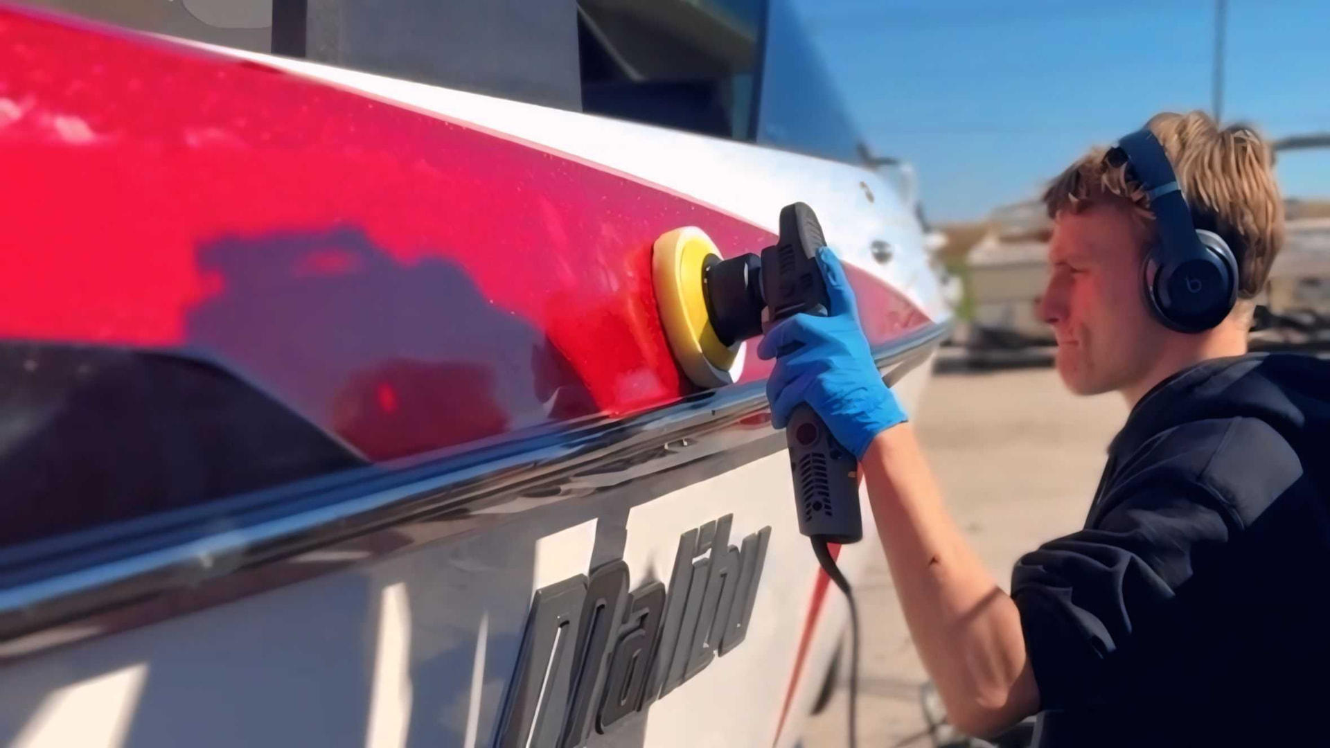 Technician machine polishing the red and white hull of a Malibu wakeboat